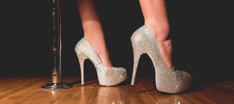 Woman's feet in sparkly high heels near a pole.