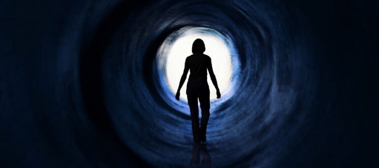 Silhouette of a woman walking toward a bright light at the end of a dark tunnel.
