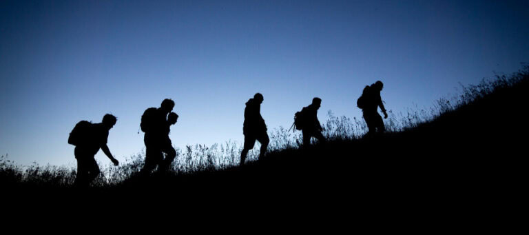 Silhouetted hikers ascend a hill at dusk.