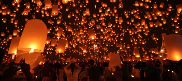 Hundreds of glowing sky lanterns rise into the night sky during a festival.