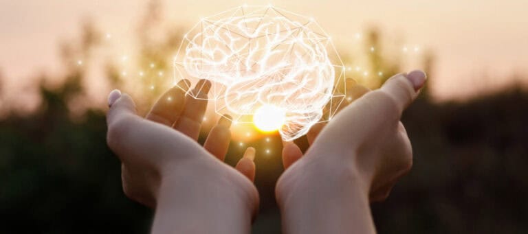 Hands gently cradling a glowing brain; a concept image representing mental health and well-being.