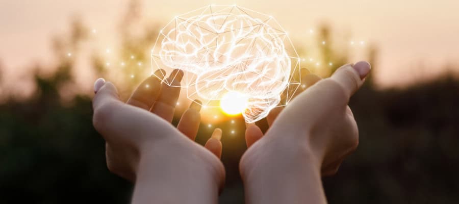 Hands gently cradling a glowing brain; a concept image representing mental health and well-being.