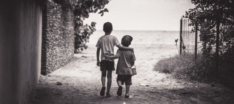 Two boys walk hand-in-hand toward the ocean.