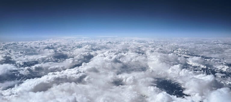 Aerial view of snow-capped mountains peeking through a vast expanse of fluffy clouds.