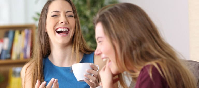 Two women laughing together over coffee, enjoying a friendly conversation.