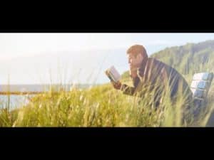 Man reading a book on a park bench overlooking the ocean. Philosophical summer reading.