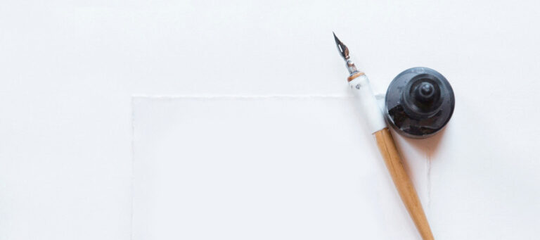 Dip pen, inkwell, and blank paper ready for writing.