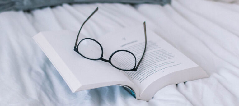 Open book with reading glasses resting on top.