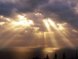 Golden sun rays breaking through dark clouds over a calm sea. Concept of God.