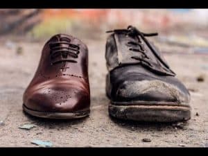 Side-by-side comparison: a polished brown dress shoe and a worn, dirty work boot. Illustrates class disparity.