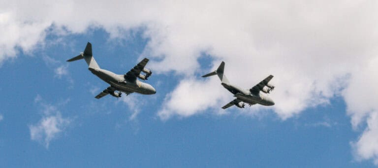 Two military transport planes flying in formation against a cloudy sky.