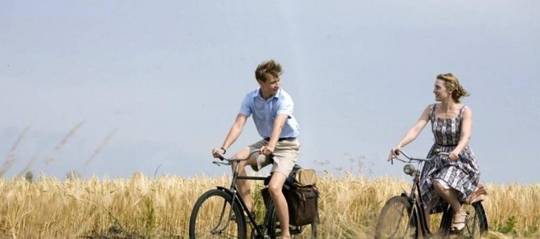 A man and woman ride bicycles through a field of wheat.