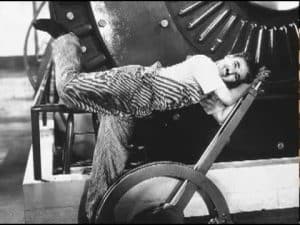 Charlie Chaplin playfully resting on industrial machinery, embodying hard work.