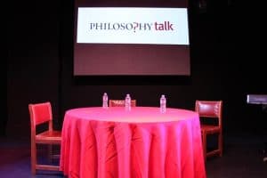 Red table set for a Philosophy?Talk live event with water bottles and chairs.