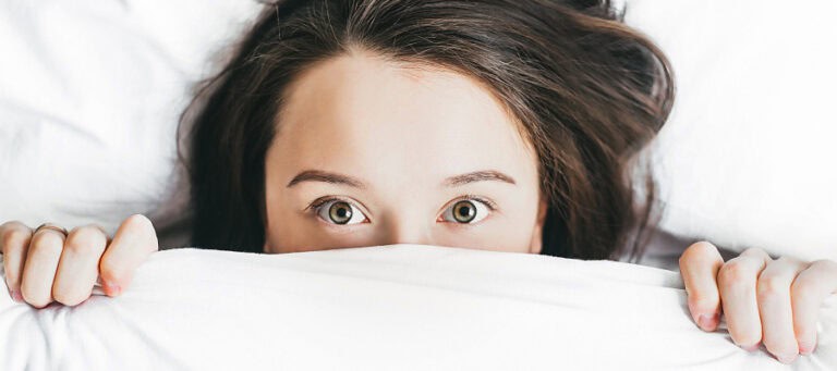 Woman's eyes peering from under white sheets.