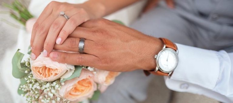 Newlywed couple's hands clasped over wedding bouquet.