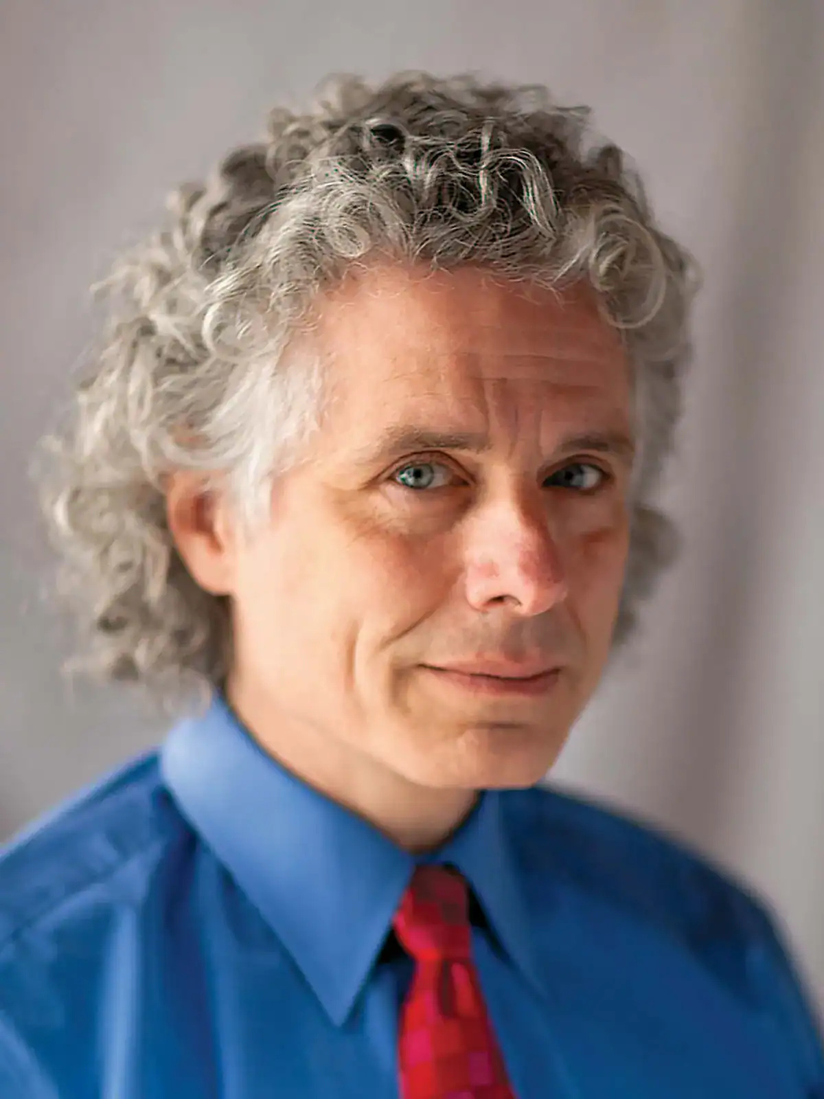 Portrait of a man with gray, curly hair, wearing a blue shirt and red tie.