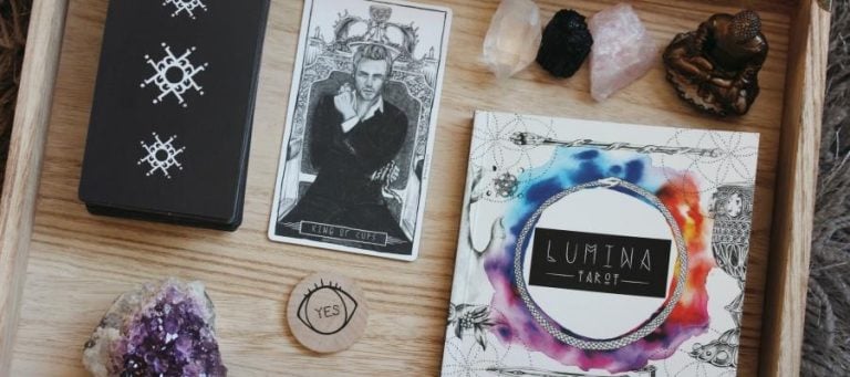 Tarot cards, crystals, and a Lumina Tarot guidebook arranged on a wooden tray. King of Cups card visible.