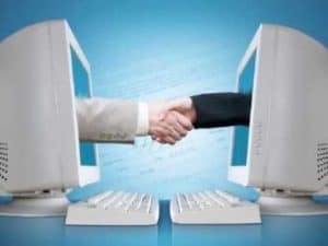 Two hands shaking across computer screens, symbolizing online networking and social connections.