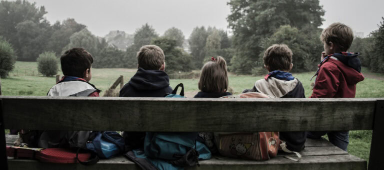 Five children sit on a park bench, facing away from the camera.