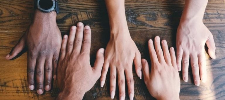 Four hands of diverse skin tones resting on a wooden surface, symbolizing unity and inclusion.