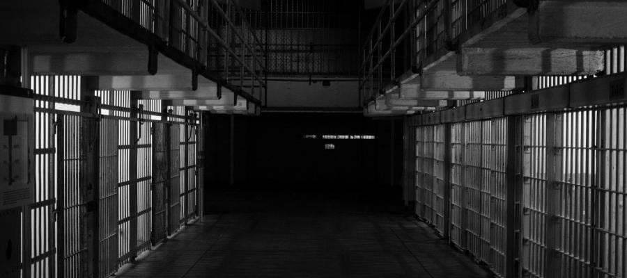 Dark prison corridor with barred cells.