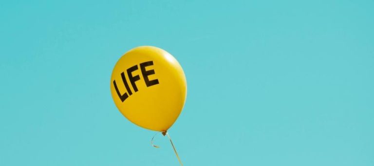 Yellow balloon with the word "LIFE" printed on it floats against a blue sky.