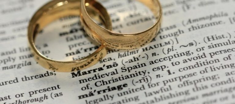 Two gold wedding rings on a dictionary page open to the definition of "marriage".