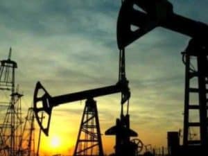 Silhouetted oil derricks at sunset; environmental impact of oil extraction.