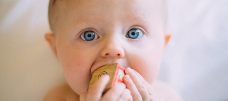 Baby with bright blue eyes holding a wooden block