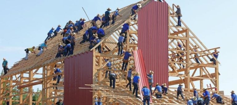 Many Amish men collaboratively build a barn's wooden frame and roof.