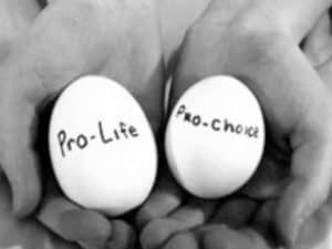 Two hands hold eggs labeled "Pro-Life" and "Pro-Choice," representing the abortion debate.