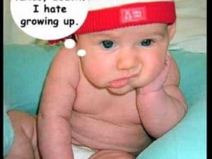 A grumpy baby in a red hat thinks "I hate growing up."