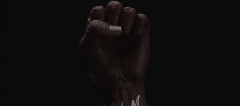 Close-up of a raised fist with "BLM" written on the wrist.