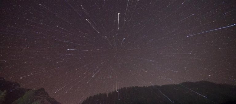 Star trails radiating from a central point over a dark mountain range at night.