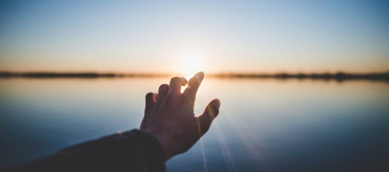 Hand reaching towards sunset over calm water. Problem of other minds.