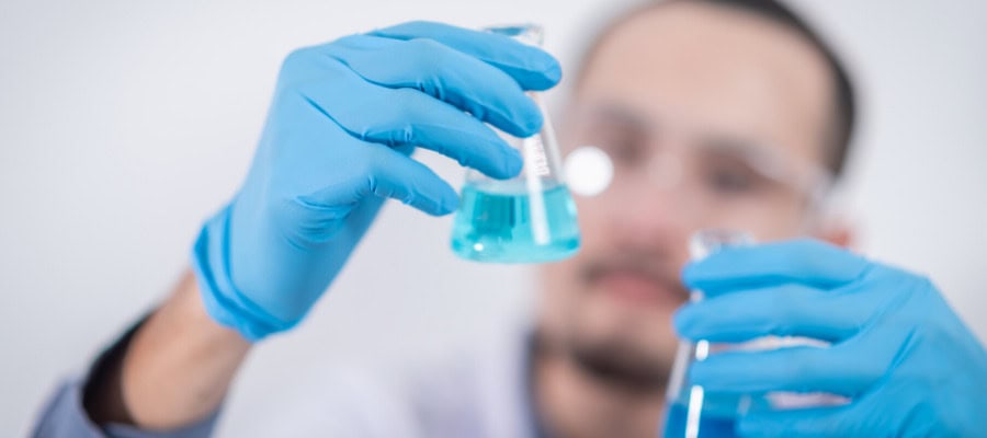 Scientist in lab coat holds beakers of blue liquid, studying the problem of other minds.