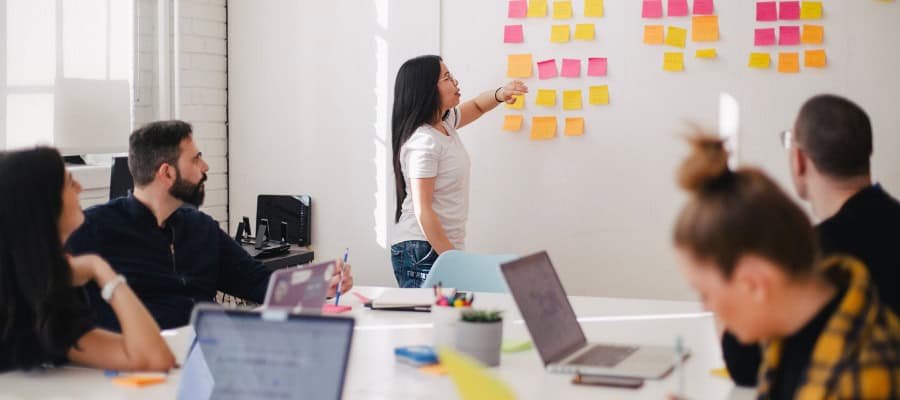 Team brainstorming, woman presenting ideas on whiteboard with sticky notes.