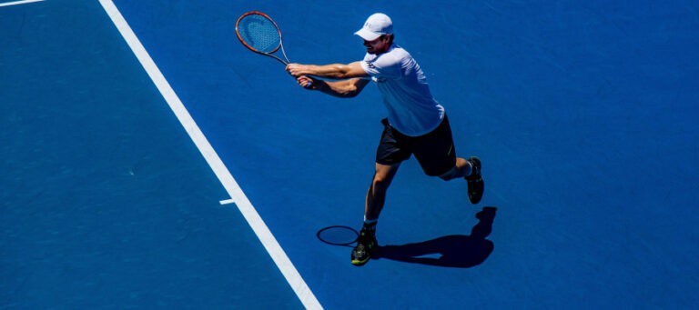 Tennis player in mid-swing on a blue court.