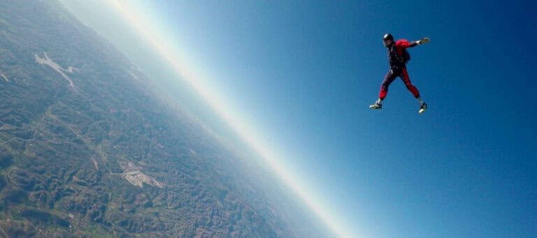 Skydiver falling through the air above a vast landscape.