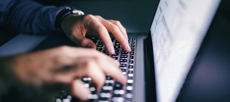 Close-up of hands typing on a laptop keyboard at night.