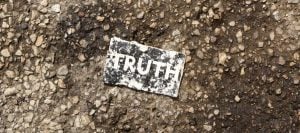 Torn piece of paper on asphalt reads "TRUTH".