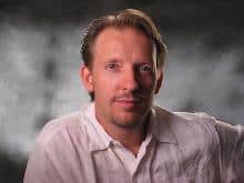 Headshot of a man with light brown hair and a goatee, wearing a light-colored collared shirt.