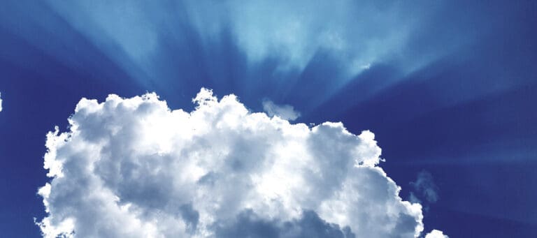 Bright sunbeams shining through fluffy cumulus clouds in a deep blue sky.