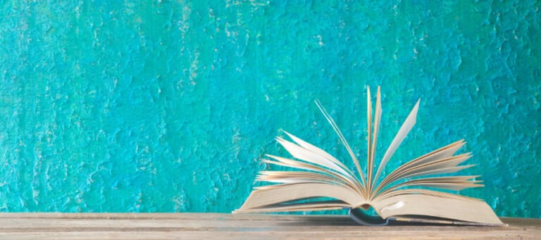 Open book on wooden surface against teal background