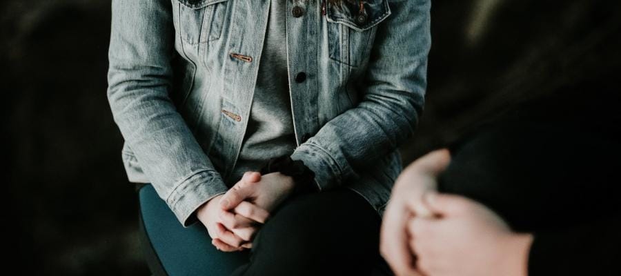 Person in denim jacket sits with hands clasped, contemplating the moral costs of climate change.