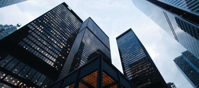 Modern skyscrapers reaching towards a cloudy sky. The moral costs of climate change are implied by the urban landscape.