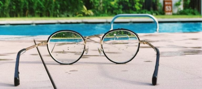 Eyeglasses resting on a pool deck, water droplets visible.