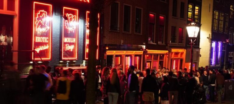 Amsterdam's Red Light District at night, with neon signs and crowds of people.