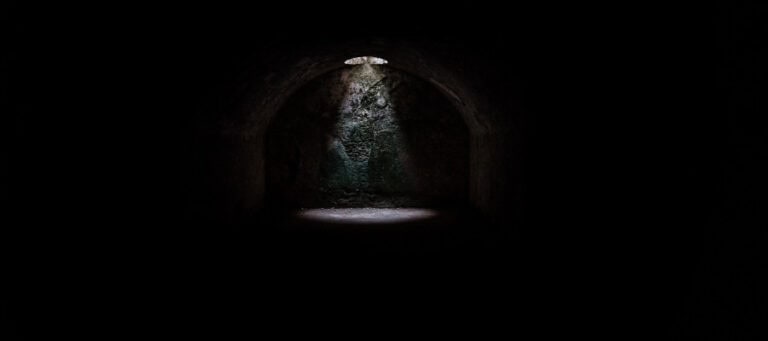 Light shining through a small opening in a dark, arched tunnel.